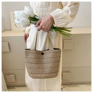 Detail of beige woven straw tote bag featuring black button closure and fabric handles