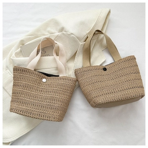 Close-up of dual-tone straw tote bags with button closure and fabric handles on art books