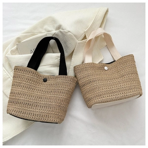 Detail of woven straw handbags with black and beige handles on a neutral fabric