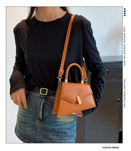 Detail of caramel brown leather handbag with geometric flap and gold metal clasp closure