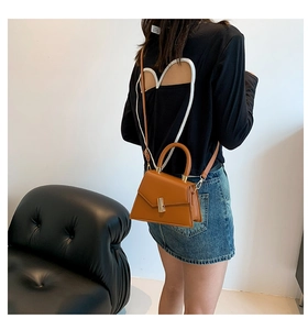 Detail of a brown trapezoid PU leather handbag with gold clasp and top handle shown on model