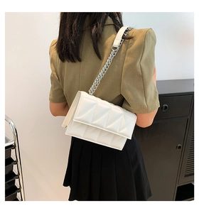 Detailed view of a white quilted leather flap bag with chain strap on a green blazer