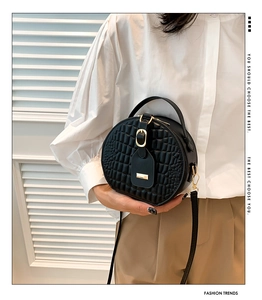 Detail einer schwarzen runden Kroko-Handtasche mit goldener Hardware und Tragegriff