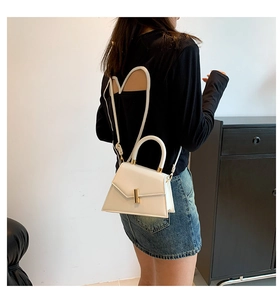 Modern white leather trapezoid bag with gold twist lock shown on a model for size scale
