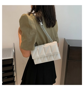 Close-up of a white quilted crossbody bag with silver chain strap worn by a model