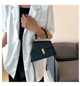 Modern black trapezoid bag with gold metal clasp shown on model wearing white blazer
