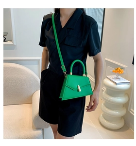 Detail of a green trapezoidal leather bag with gold buckle on a black shirt outfit
