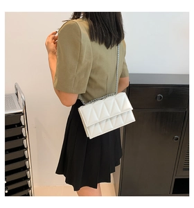 Gros plan d'un sac à bandoulière matelassé blanc avec chaîne argentée porté par un mannequin