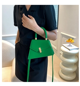 Detail of bright green trapezoid handbag with gold cylindrical buckle held by model