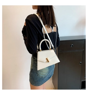 Detail of white geometric trapezoid handbag with gold cylindrical metal buckle