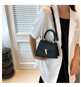 Detail of a black matte leather trapezoid handbag with a gold metal lock and shoulder strap