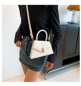 Close-up of a white trapezoid handbag featuring a gold bar lock and sleek adjustable strap