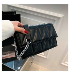 Détail d'un sac bandoulière matelassé noir avec une grosse chaîne en métal argenté