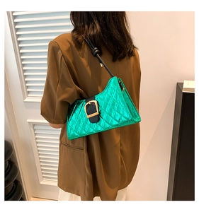 Detailed view of a metallic green quilted baguette bag with black buckle strap on a shoulder