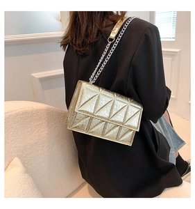 Detailed view of a gold quilted crossbody bag with metal chain strap on black blazer