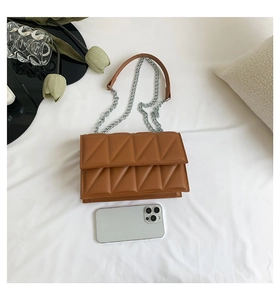 Sac bandoulière matelassé marron avec chaîne à côté d'un smartphone pour comparer la taille