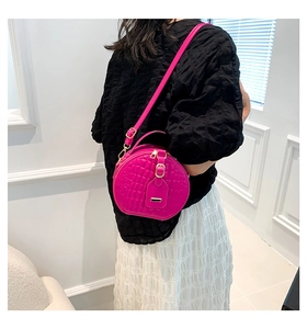 Detail der pinkfarbenen runden Tasche mit Krokoprägung, getragen von einem Modell