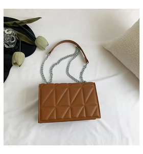 Détail d'un sac bandoulière marron matelassé avec motifs géométriques et chaîne argentée