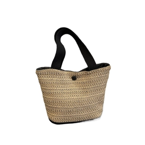 French style woven straw tote bag with black fabric handles and a snap closure for beach