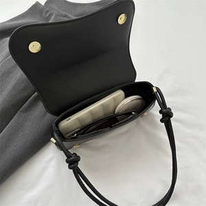 Minimalist black leather crossbody bag with magnetic closure and knotted strap details
