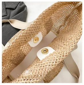 Detail of woven straw tote bag featuring white leather trim and gold magnetic buckle closure