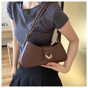 Detail of a brown half-moon baguette bag with round dual-tone metal buckle and knotted strap