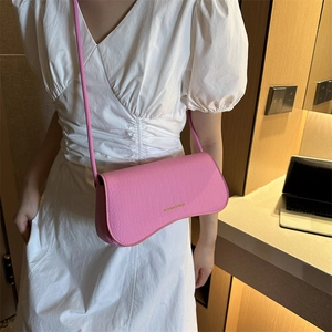 Pink faux leather shoulder bag with crocodile texture and gold lettering on white dress