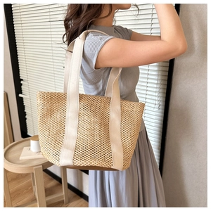 Detail of woven straw beach tote bag with cream fabric strap and leather base reinforcement