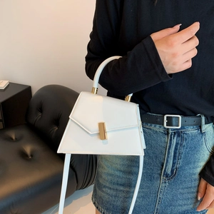 Minimalist white leather crossbody bag with gold buckle in a lifestyle setting