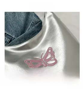 Detail of silver metallic PU bag featuring pink embroidered butterfly and lychee texture