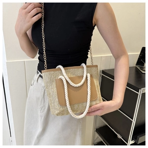 Detail der Stroh-Eimertasche mit beigem Webmuster und einer braunen Leder-Fronttasche