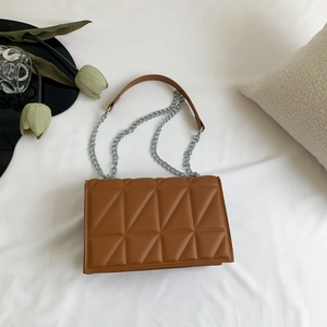 Petit sac à bandoulière marron matelassé avec chaîne argentée sur fond de tissu blanc