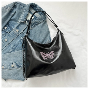 Detail of black faux leather handbag with pink butterfly embroidery and metal chains