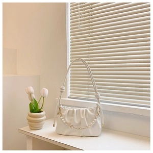 Detail of white pleated cloud bag with elegant pearl and floral chain decoration