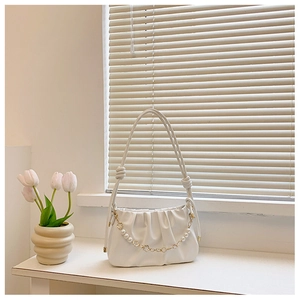 Detail of white pleated cloud bag with pearl chain and golden clover charms on a windowsill