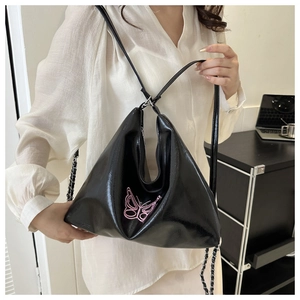 Detail of a black shiny PU triangle bag with pink butterfly embroidery on a leather strap