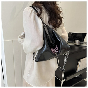Detail of black patent leather bag featuring pink butterfly embroidery and chain strap