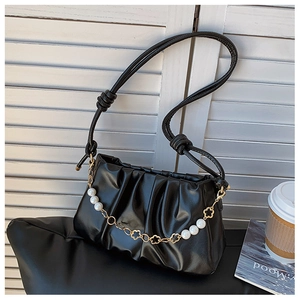 Close-up of black pleated cloud bag with elegant pearl and gold flower chain detail