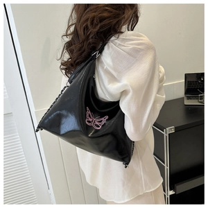 Macro detail of glossy black moon bag featuring pink butterfly embroidery and metal chain