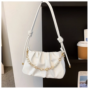 Detail of white pleated cloud bag featuring decorative pearl and gold flower chain strap