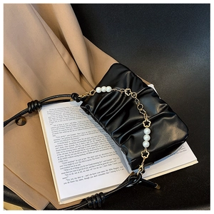 Detail view of ruched cloud bag with pearl chain and gold floral accents on vintage book