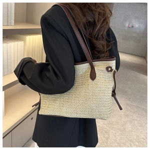 Détail du sac cabas en paille avec bandoulière en cuir brun sur l'épaule du modèle