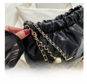 Detail of gold chain and metal hook with spherical pendant on black quilted bag