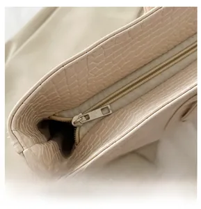 Close-up of the smooth silver zipper on a beige crocodile pattern embossed tote bag