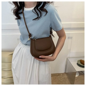 Détail du sac bandoulière en cuir marron foncé sur mannequin avec pull bleu