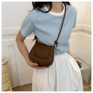 Détail d'un sac bandoulière marron semi-circulaire avec nœud décoratif sur la sangle