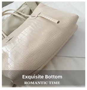 Detail view of the wide bottom base of the beige crocodile pattern tote bag