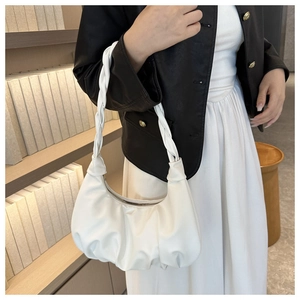 Close-up of white pleated dumpling bag with woven strap worn by a model in soft light
