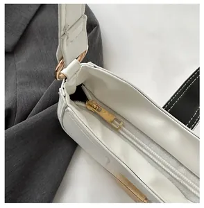 Detail view of smooth golden zipper and metal ring hardware on white PU shoulder bag