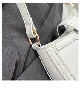 Close-up of golden circular metal hardware and stitching on a white PU shoulder bag